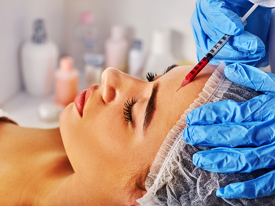Filler injection for woman forehead face. Plastic aesthetic facial surgery by doctor in beauty clinic. Doctor in medical gloves with syringe. Removing wrinkles with help of new technologies such as botox or fillers.