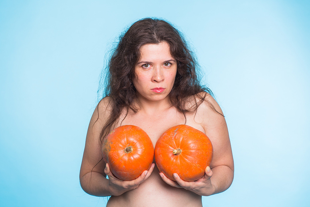 woman with two pumpkins strategically held over chest, considering breast reduction surgery